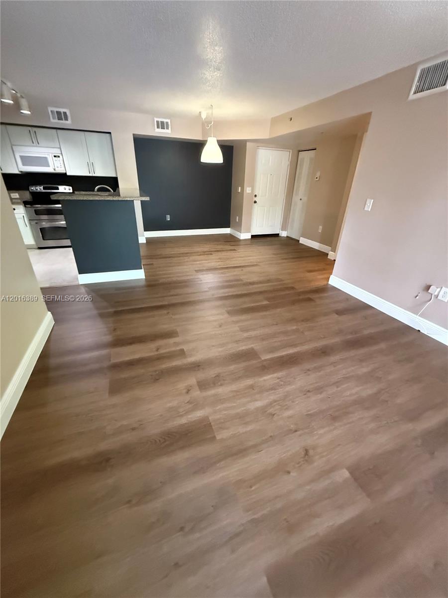 2113 Renaissance Boulevard, Unit 203 Miramar, FL 33025 - Photo 6 of 19 an empty room with wooden floor and kitchen view