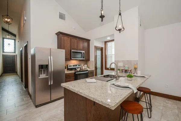 a kitchen with stainless steel appliances granite countertop a sink a stove a refrigerator cabinets a dining table and chairs