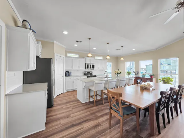 a kitchen with stainless steel appliances kitchen island granite countertop a stove a refrigerator a sink a dining table and chairs with wooden floor