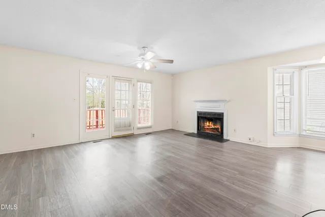 an empty room with wooden floor fireplace and windows