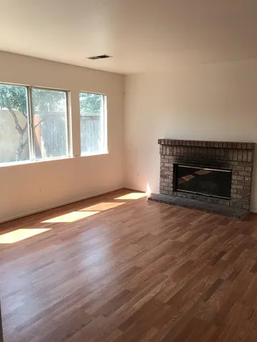 an empty room with wooden floor fireplace and windows