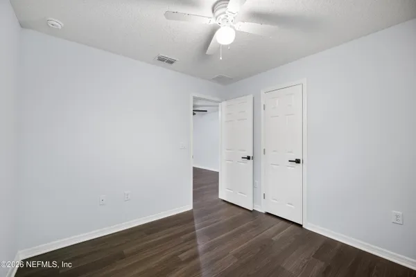 a view of an empty room with wooden floor and a ceiling fan