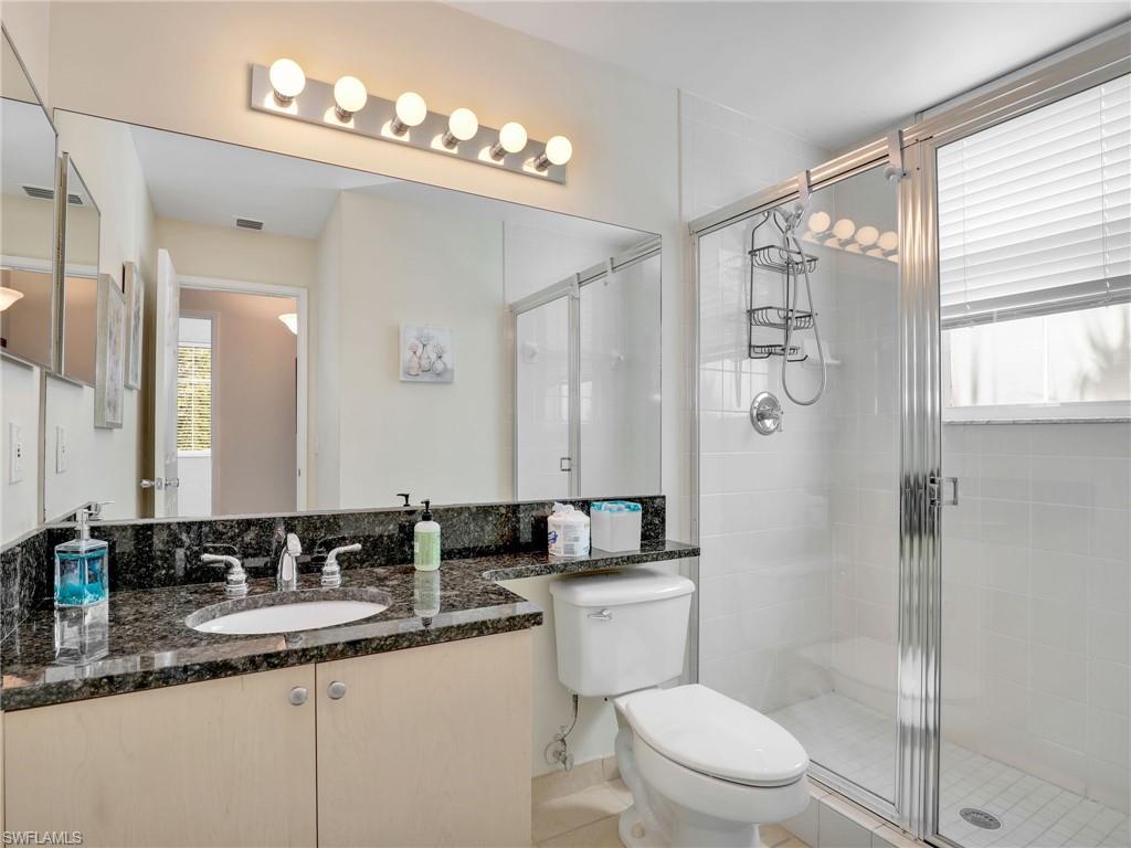 1205 Reserve Way, Unit 302 Naples, FL 34105 - Photo 20 of 31 a bathroom with a granite countertop sink a mirror a toilet and shower