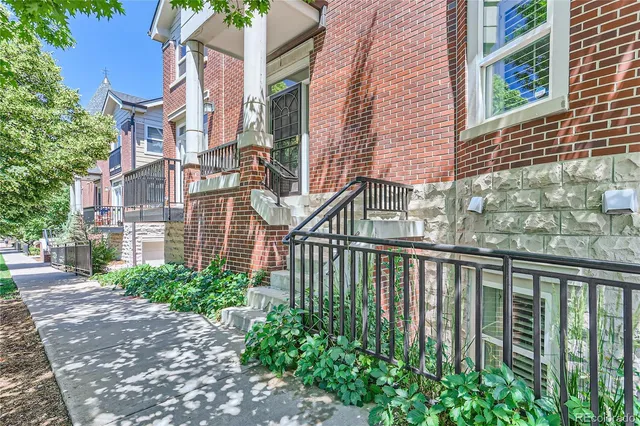 a view of a brick house with many windows plants and large trees