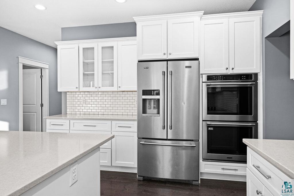3879 Okerstrom Road Hermantown, MN 55811 - Photo 8 of 32 Kitchen with stainless steel appliances, white cabinetry, glass insert cabinets, light stone counters, and tasteful backsplash