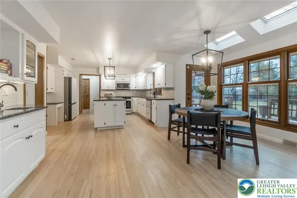 a kitchen with stainless steel appliances kitchen island granite countertop a stove a refrigerator a dining table and chairs with wooden floor