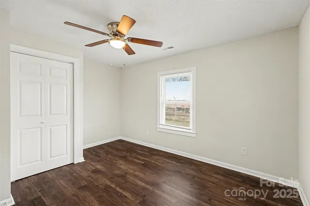 an empty room with wooden floor ceiling fan and windows
