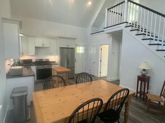 a kitchen with stainless steel appliances kitchen island granite countertop a dining table chairs and a refrigerator