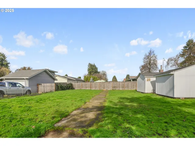 a view of a white house next to a yard with big trees