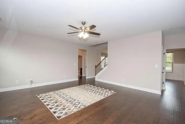 a view of an empty room with wooden floor and a ceiling fan