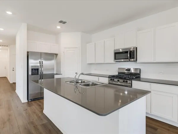 a kitchen with stainless steel appliances granite countertop a sink a stove top oven a refrigerator and dishwasher with wooden floor