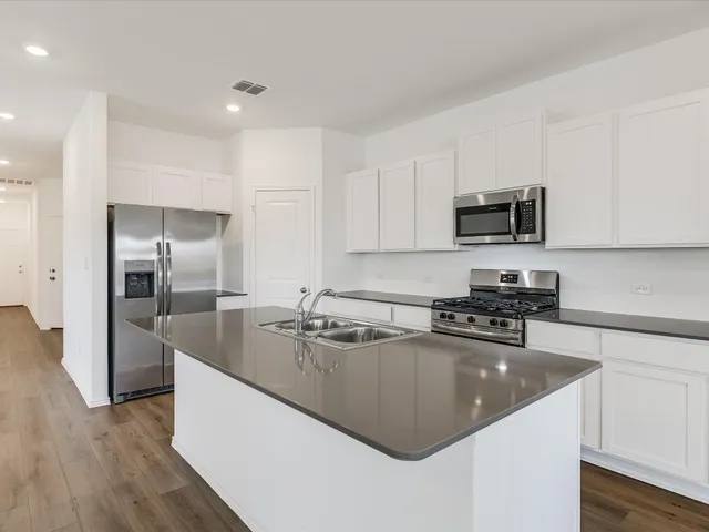 a kitchen with stainless steel appliances granite countertop a sink a stove top oven a refrigerator and dishwasher with wooden floor