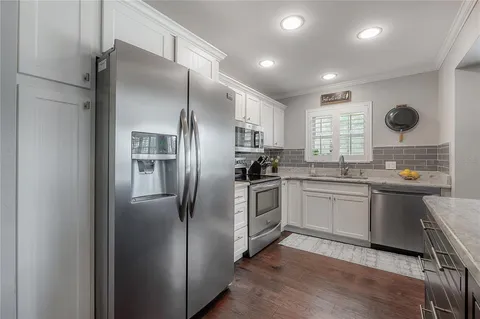 a kitchen with stainless steel appliances granite countertop a refrigerator a sink a stove and white cabinets