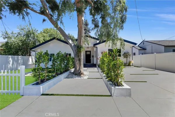 a view of a house with a small yard plants and a large tree