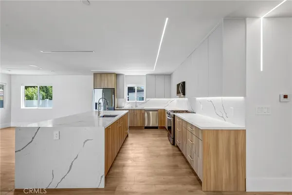 a large open kitchen with kitchen island a sink dishwasher a refrigerator and a stove with wooden floor