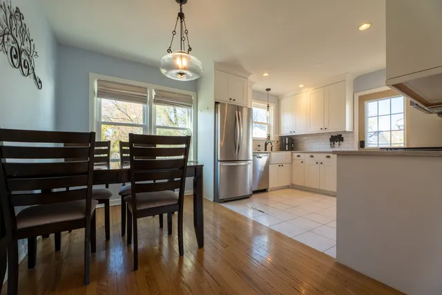 a kitchen with stainless steel appliances kitchen island granite countertop a refrigerator a stove a sink a dining table and chairs with wooden floor