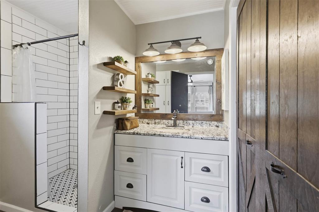 308 West 1st Street Springtown, TX 76082 - Photo 23 of 39 Bathroom featuring a white vanity with a granite-style countertop, a wood-framed mirror, and a three-light vanity fixture