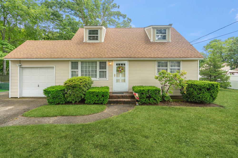 Cape cod home with a garage, a front yard, roof with shingles, and driveway