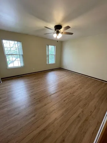 an empty room with wooden floor chandelier fan and windows