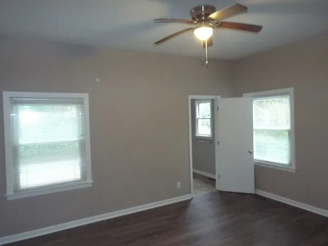 an empty room with wooden floor closet and windows