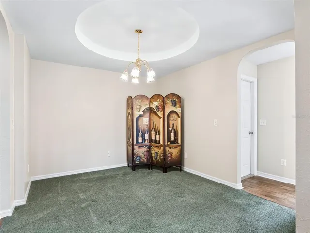 a view of an empty room with chandelier and a kitchen