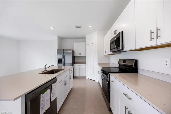 a kitchen with stainless steel appliances a stove a sink a stove top oven a refrigerator a sink and dishwasher with white cabinets