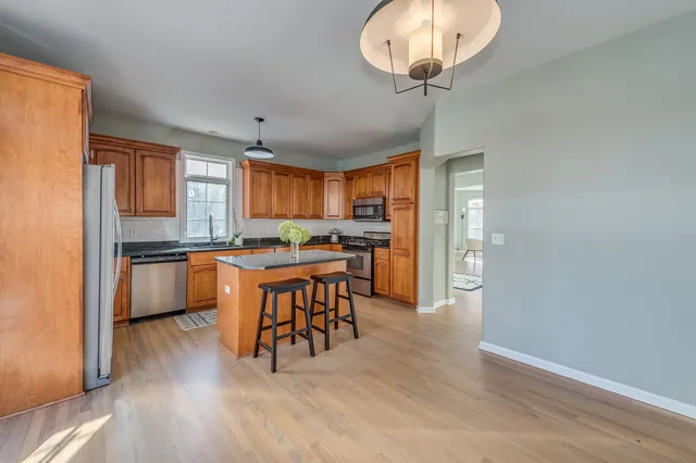 a kitchen with stainless steel appliances granite countertop a stove top oven a sink dishwasher a dining table and chairs with wooden floor