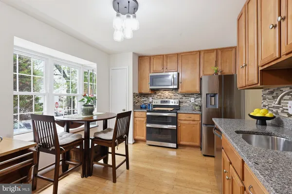 a kitchen with stainless steel appliances granite countertop a stove a refrigerator a sink a dining table and chairs with wooden floor