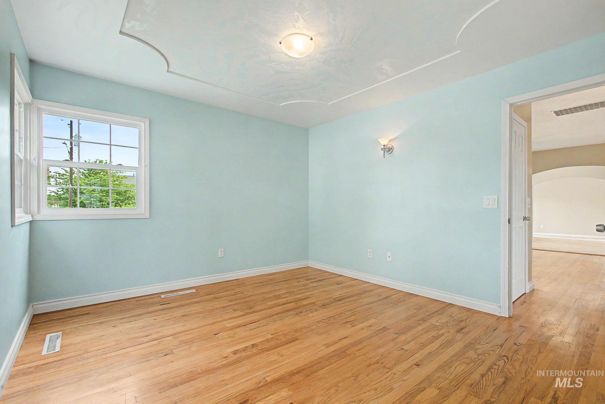 3314 6th Street Lewiston, ID 83501 - Photo 19 of 50 Hardwood flooring featuring a light tone, ceiling light fixture, wall sconce lighting, window with exterior landscaping, and a tray ceiling detail