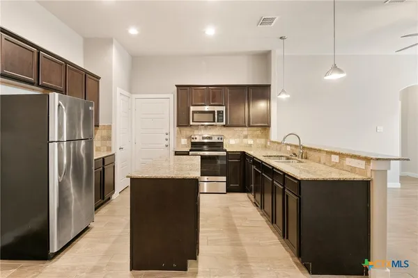 a kitchen with stainless steel appliances granite countertop a refrigerator a stove and a sink