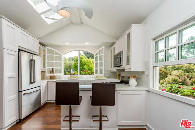 a kitchen with stainless steel appliances granite countertop a stove a refrigerator a sink a dining table and chairs with wooden floor