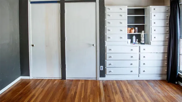 an empty room with wooden floor and windows with curtains