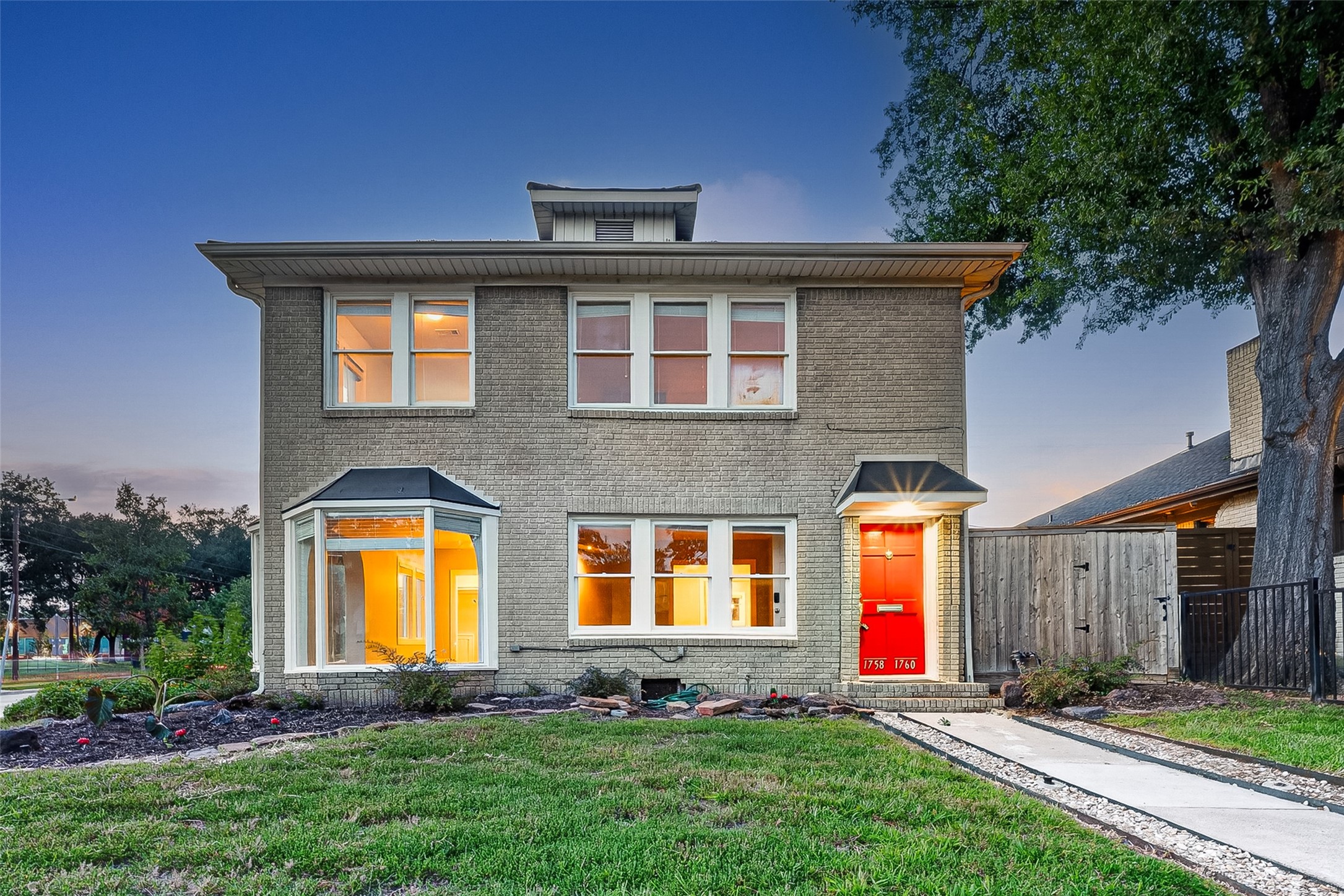 1758 Hawthorne Street, Unit 2 Houston, TX 77098 - Photo 2 of 19 This charming two-story home features a classic brick exterior with large windows and a vibrant red front door. The property includes a well-maintained front lawn, a pathway, and mature trees, offering a welcoming and inviting curb appeal.