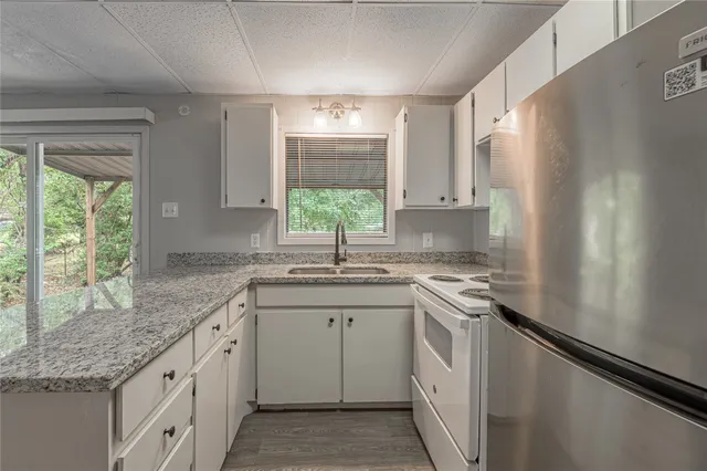 a kitchen with granite countertop white cabinets white appliances a sink and a large window