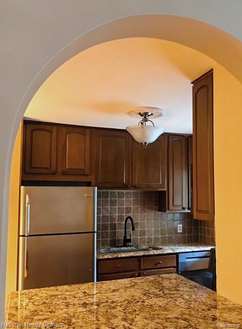 475 South Adams Road, Unit 19 Birmingham, MI 48009 - Photo 7 of 20 Archway entry to kitchen with stainless steel refrigerator, dark wood cabinetry, tile backsplash, and speckled countertops