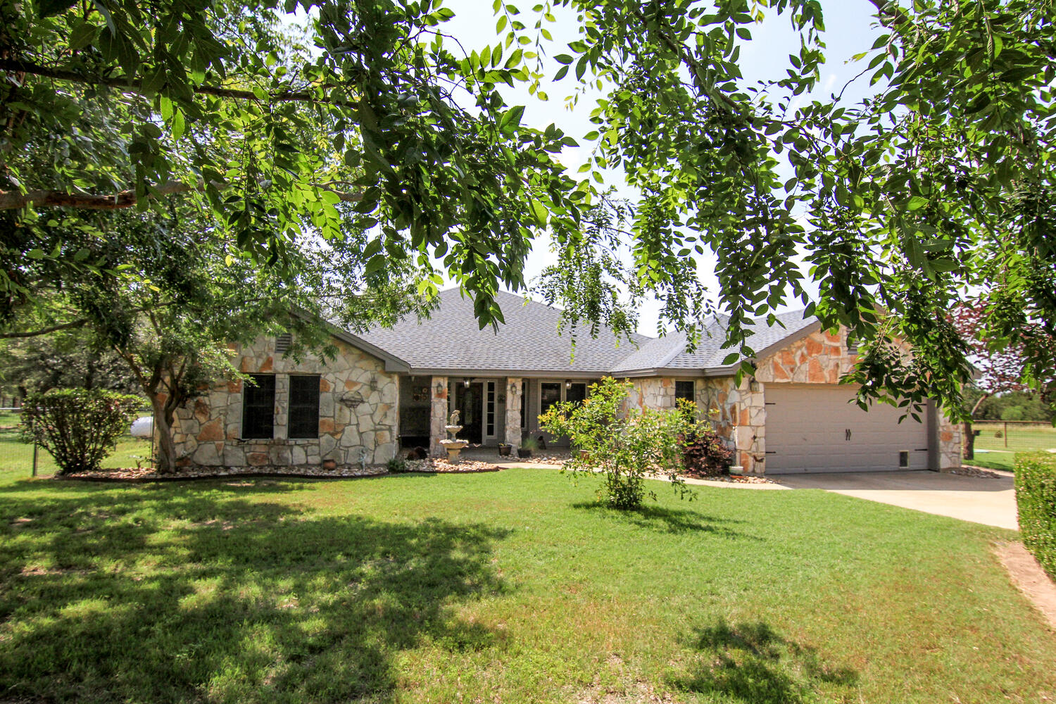 Ranch-style house with stone siding, a front yard, circle driveway, and a garage