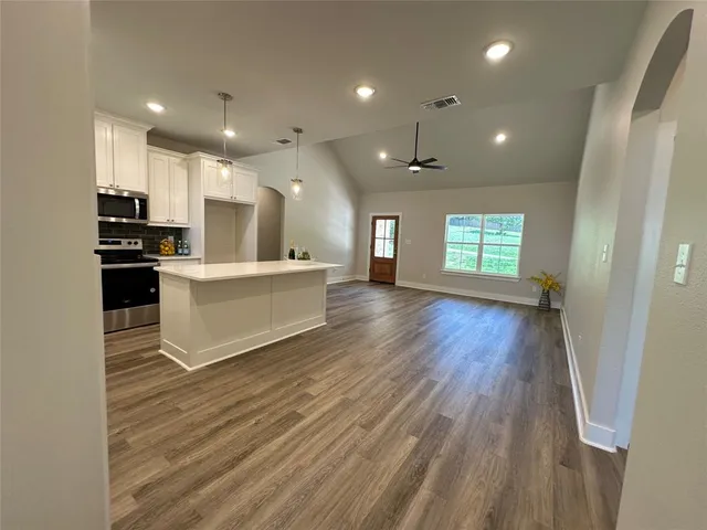 a large white kitchen with kitchen island a sink dishwasher a refrigerator and a stove with wooden floor