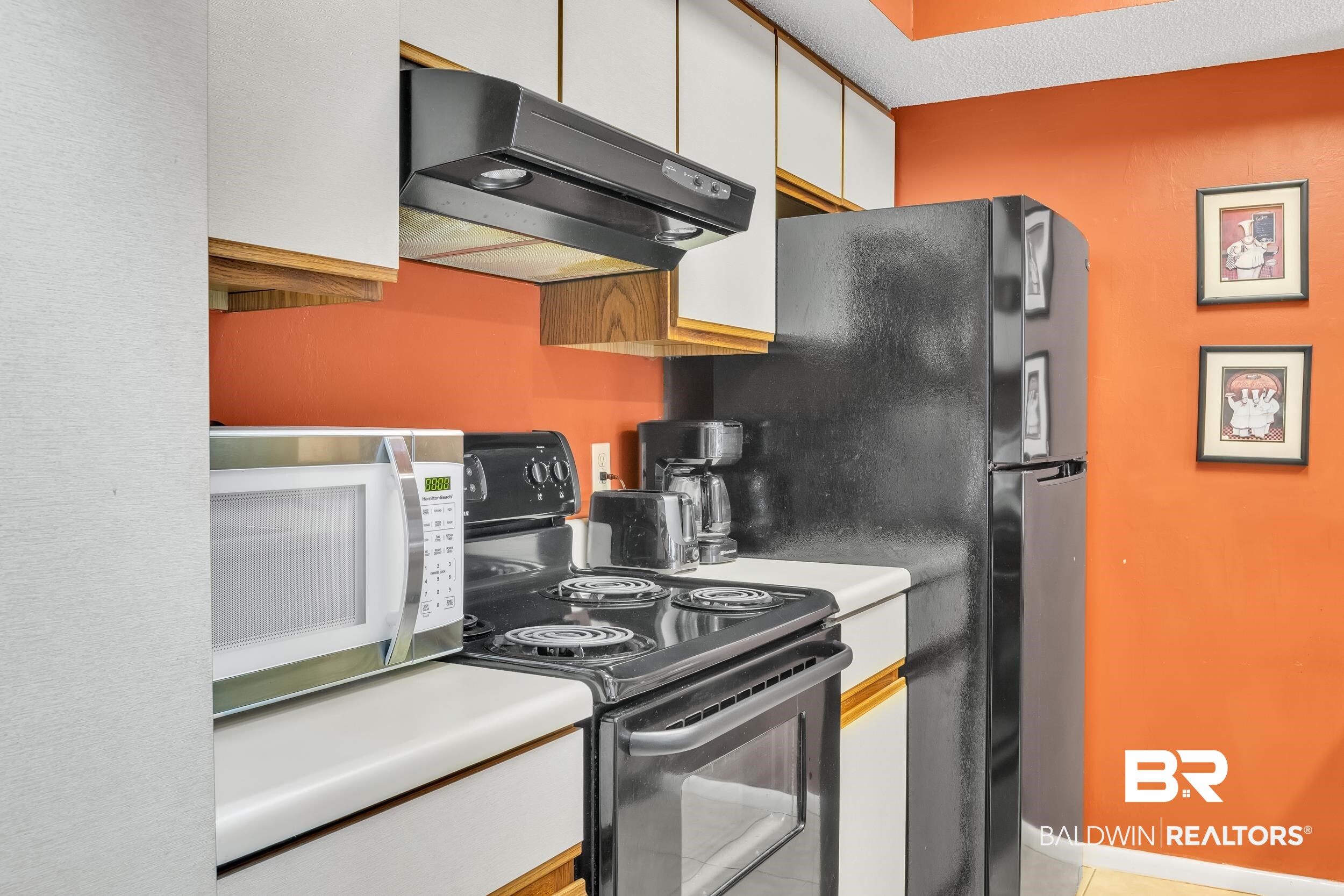 3256 Loop Road, Unit 2 Orange Beach, AL 36561 - Photo 17 of 25 Kitchenette featuring white cabinetry, a black range with an overhead vent, a black refrigerator, and a light-toned countertop