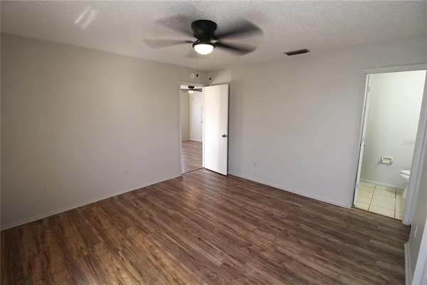 a view of an empty room with wooden floor and a ceiling fan