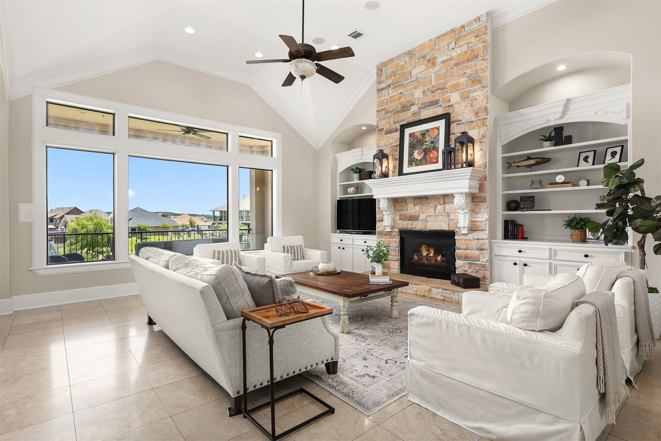 10896 Decatur Street Willis, TX 77318 - Photo 25 of 50 This spacious living room boasts a high ceiling with a fan, a cozy stone fireplace, and built-in shelves, all bathed in natural light from large windows that offer a scenic view, while the neutral palette and elegant furniture create a welcoming and sophisticated atmosphere.