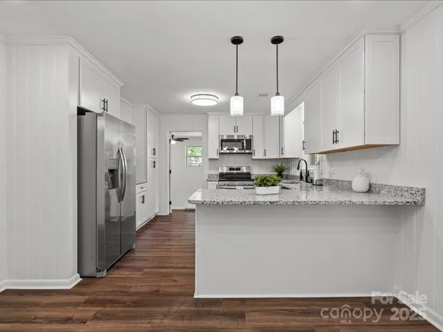 a kitchen with stainless steel appliances granite countertop a refrigerator a sink dishwasher a stove and white cabinets with wooden floor