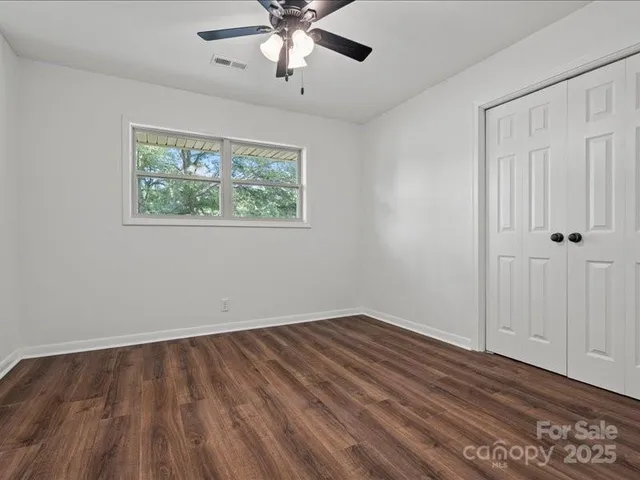 an empty room with wooden floor chandelier fan and windows
