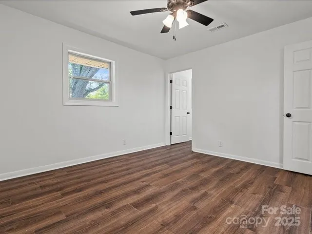 a view of an empty room with wooden floor and a ceiling fan