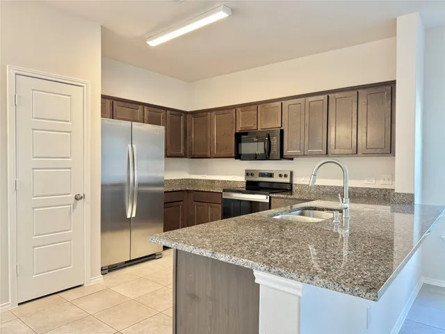 a kitchen with stainless steel appliances granite countertop a refrigerator a stove and a sink with wooden floors
