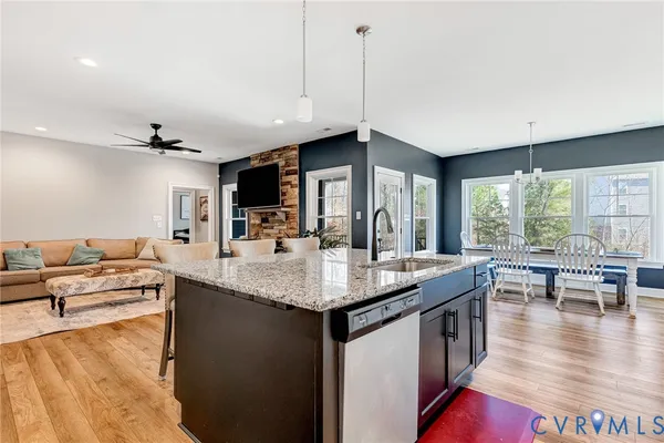 a living room with stainless steel appliances granite countertop a sink dishwasher and a flat tv screen next to a large window with wooden floor