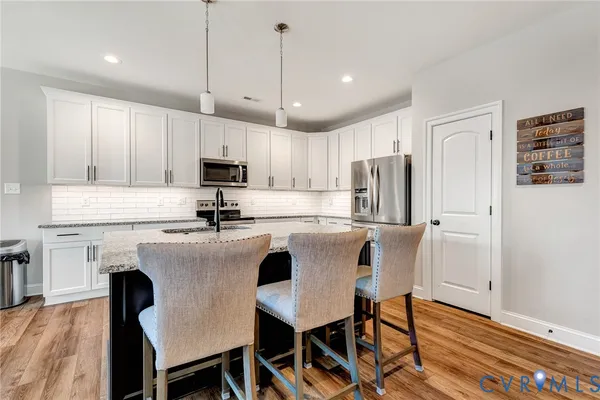 a kitchen with stainless steel appliances granite countertop a stove a refrigerator a microwave a sink and white cabinets with wooden floor