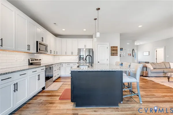 a large kitchen with stainless steel appliances kitchen island granite countertop a stove a sink a refrigerator and white cabinets