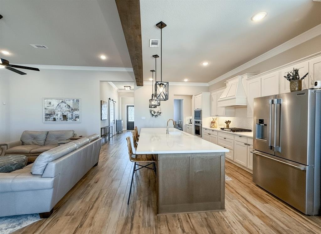 12116 Magma Court Krum, TX 76249 - Photo 9 of 30 a large kitchen with stainless steel appliances kitchen island granite countertop a refrigerator a oven a island and couches with wooden floor