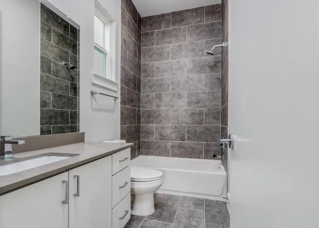 a bathroom with a granite countertop bathtub shower sink vanity and toilet