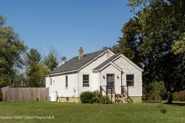 a view of a white house next to a yard and large trees